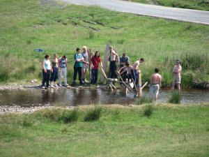 Team of young people building a bridge across a river near Dolydd.